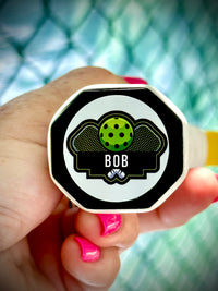 Hand holding a personalized pickleball paddle tag with the name Bob