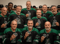 Hockey team in green jerseys posing with custom team pucks in a locker room