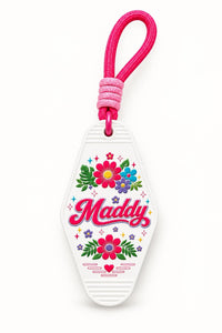 White retro motel-style keychain with colourful floral artwork, the name Maddy in pink script and a pink paracord strap